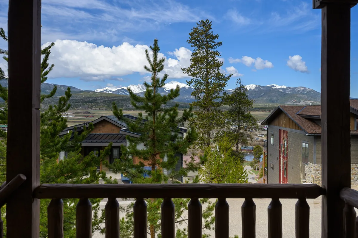 A tranquil view of snow-capped mountains framed by pine trees and modern buildings below, suggesting a vibrant mountain town atmosphere. This scene transitions naturally between outdoor adventure and the comforts of the resort area.
