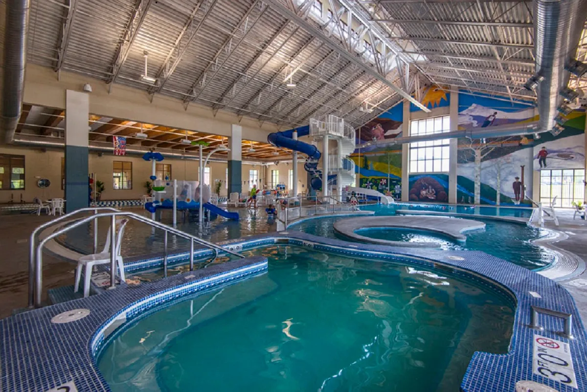 An energetic indoor scene featuring a swimming pool with water slides, children playing, and colorful murals, evoking a sense of fun and excitement perfect for family outings. The space is bright and lively, ideal for memorable summer experiences.