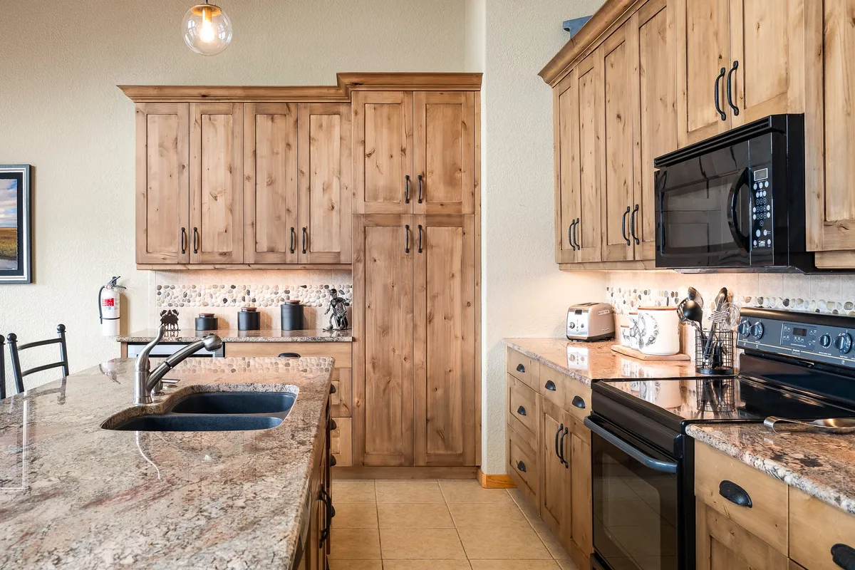 A modern kitchen with gleaming granite countertops, rich wood cabinetry, and high-end appliances. The kitchen island provides additional workspace and seating, emphasizing both function and hospitality. The atmosphere feels cozy yet upscale, ideal for family meals and culinary creativity.