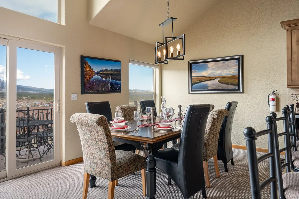 A warm, inviting dining area centered around a custom wood table with elegant chairs. Large windows bathe the room in natural light, and tasteful artwork adorns the walls. The space is set for group dining and lively gatherings, echoing the section's emphasis on communal meals and celebration.
