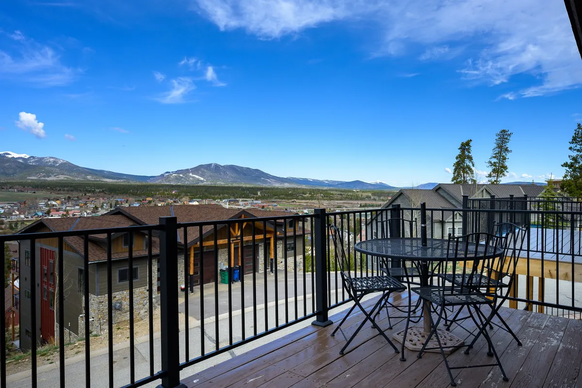 An outdoor deck space with a balcony railing, table and chairs, and a breathtaking mountain view. The setup is perfect for enjoying morning coffee, al fresco meals, or stargazing, seamlessly connecting the indoor living space to the outdoors.