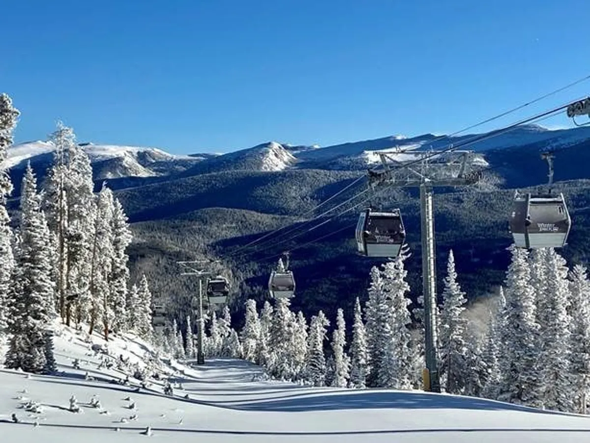 A breathtaking exterior shot of ski lift gondolas gliding above snow-covered trees and majestic mountain peaks. The scene is serene yet invigorating, emphasizing the allure of winter sports and mountain scenery.