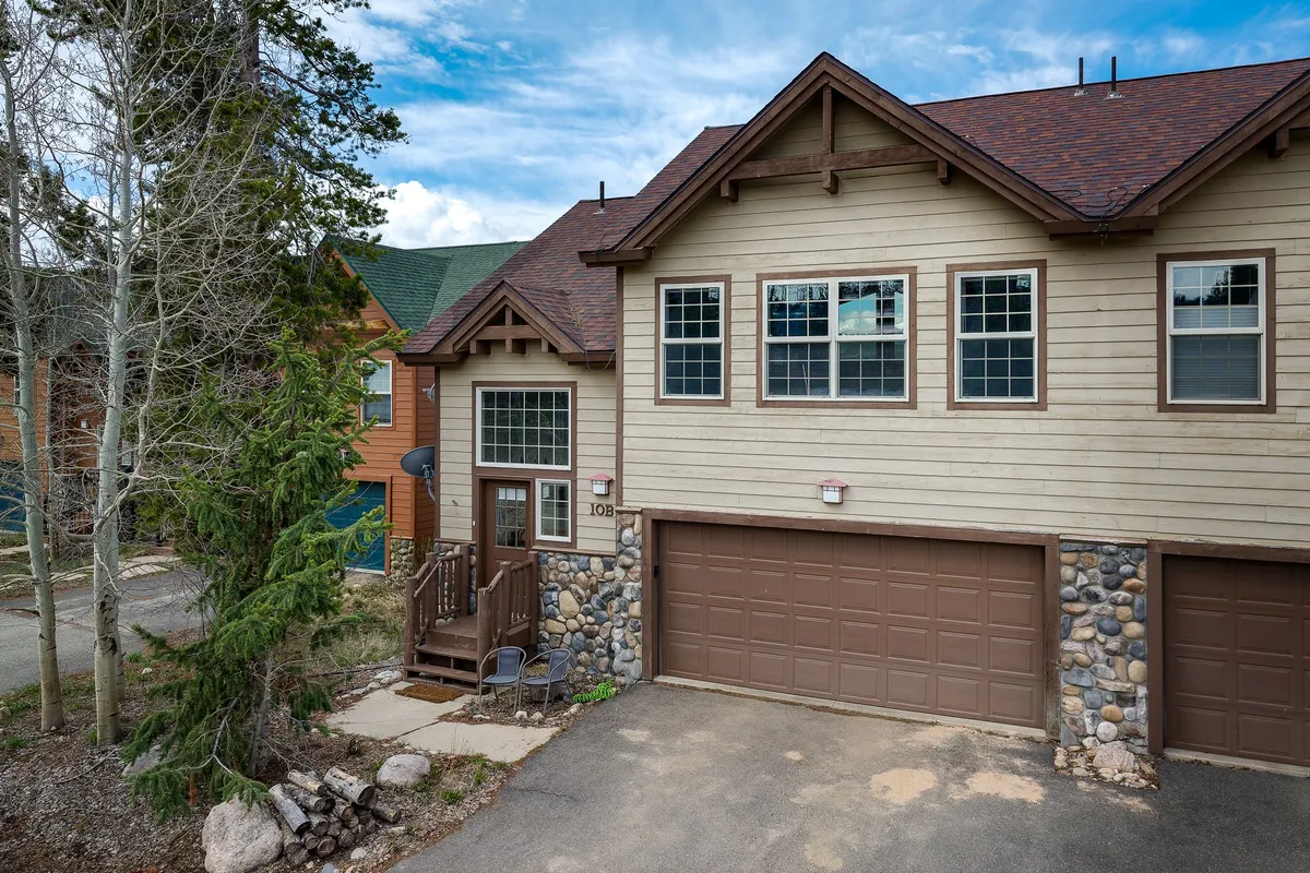 The exterior view features the villa’s inviting front entrance, prominent stone facade, and attached garage door, all set within a landscaped area. This image gives a clear sense of how the garage connects to the home and the outdoors, emphasizing easy access for loading and unloading gear.
